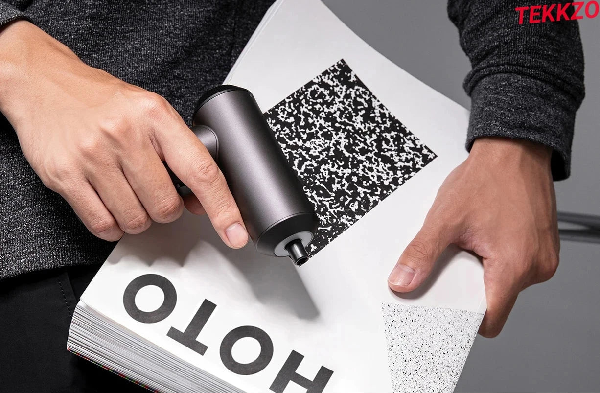 Hands holding a modern ink roller applying black ink over a white book page with bold text and patterns