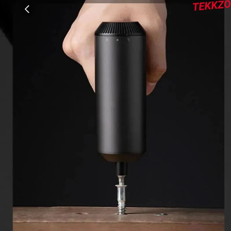 Hand holding black electric screwdriver driving screw into wood on dark background